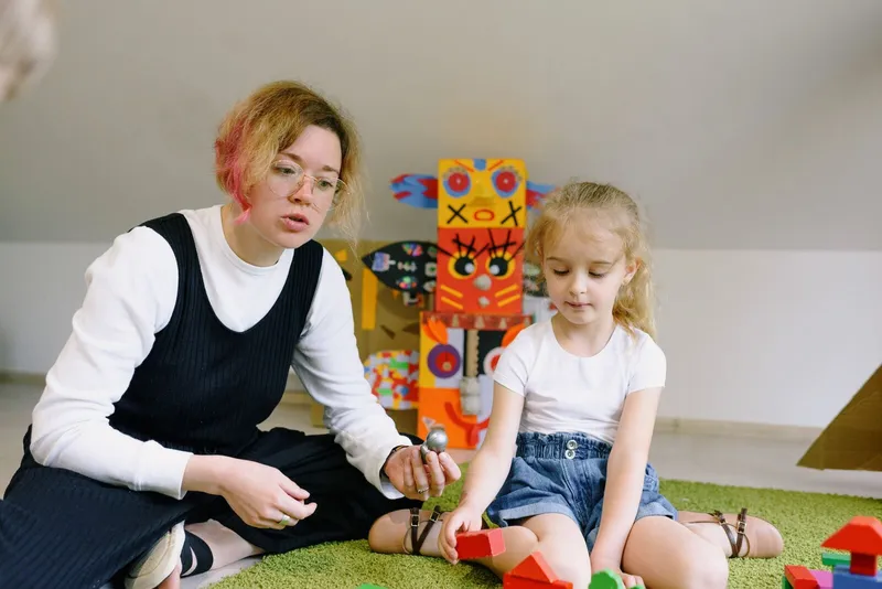 Terapeuta e menina sentadas em um tapete verde brincando com blocos de madeira coloridos